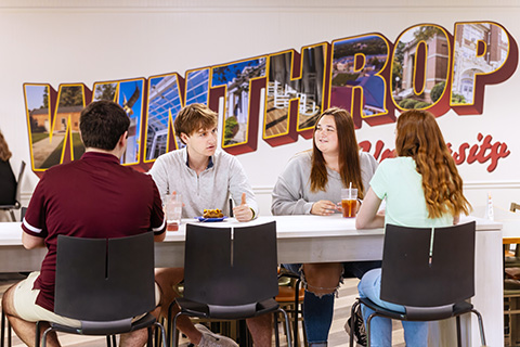 a group of students eating lunch together with a Winthrop mural behind them