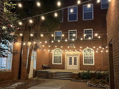 Glowing lights strung up in trees around brick courtyard