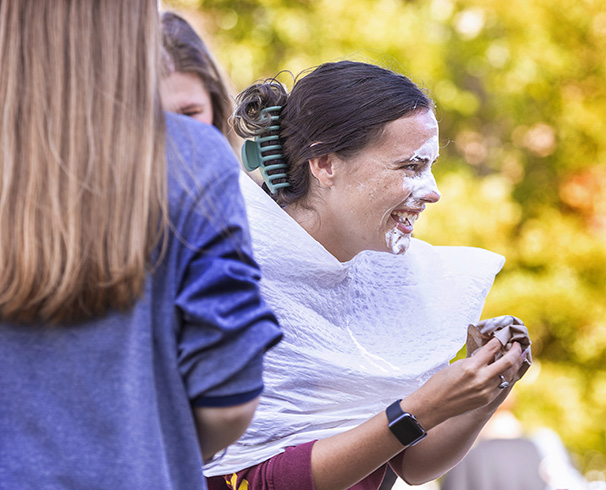 a student laughing after being hit with a pie at an event