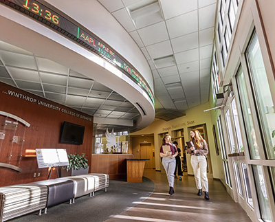 two students walking past the stock ticker in Carroll Hall