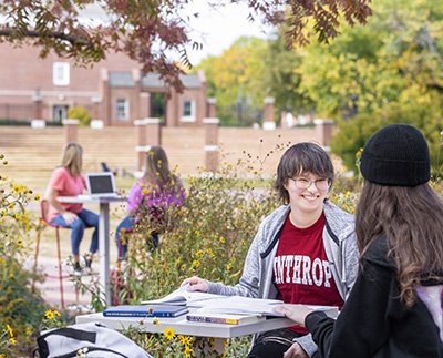 students sitting outside and studying at high top tables surrounded by flowers