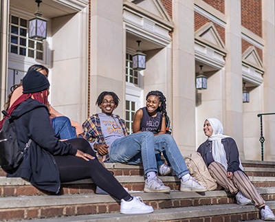 a group of students sitting on the steps of Byrnes Auditorium and laughing together