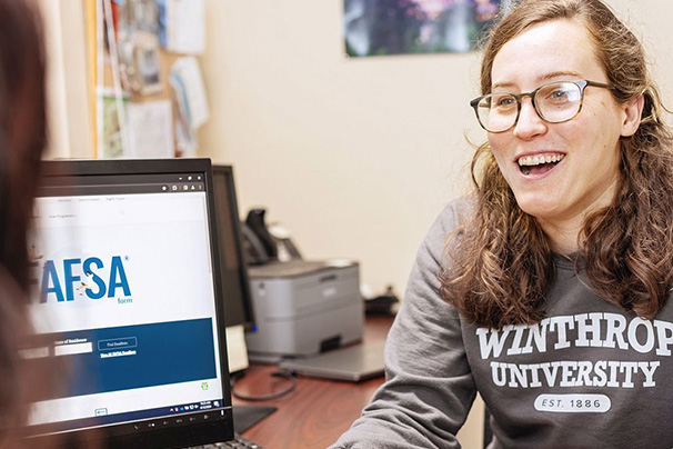 a financial aid counselor explaining the tuition process to a student with the FAFSA
                  website up on the computer screen