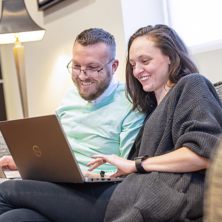 two adult students sitting on a couch and working on their laptops