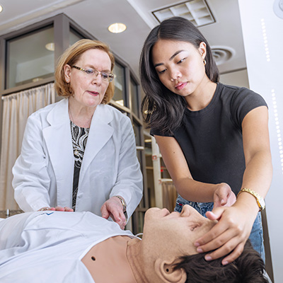 Professor guiding a student as they work on a manikin