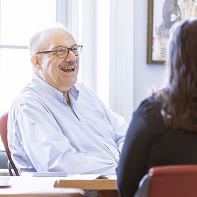 Older man laughing at a desk with art in the background