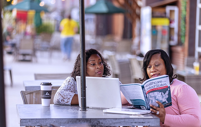 Two adult students working on a laptop at a coffee shop