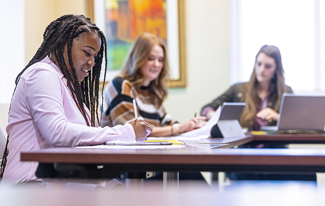 Three graduate students at a table working on assignments