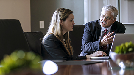 A man and woman in business attire working with a laptop on a conference table