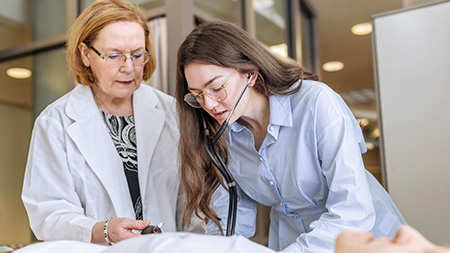 A professor working with a student wearing a stethoscope