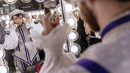 A student actor in costume finishing their makeup in the dressing room