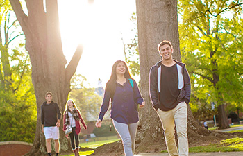 Four smiling students walking across the front lawn of campus